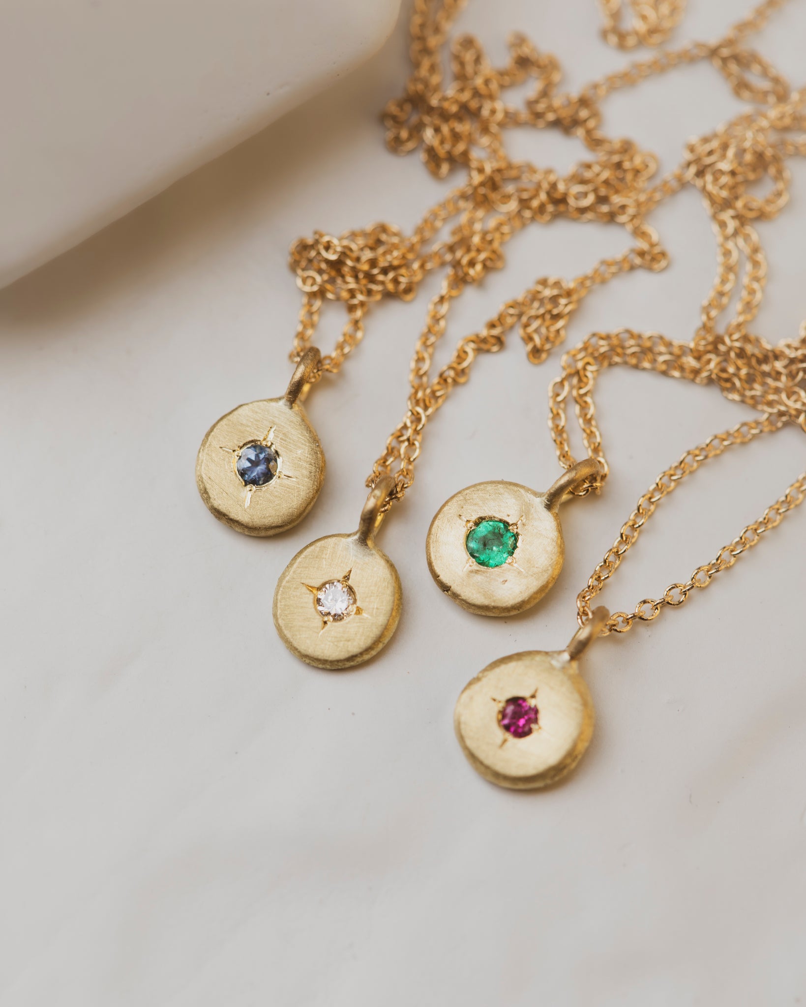 18K yellow gold pebble gemstone necklaces with a diamond, sapphire, emerald or ruby in the center. 5mm round with 2mm gemstone