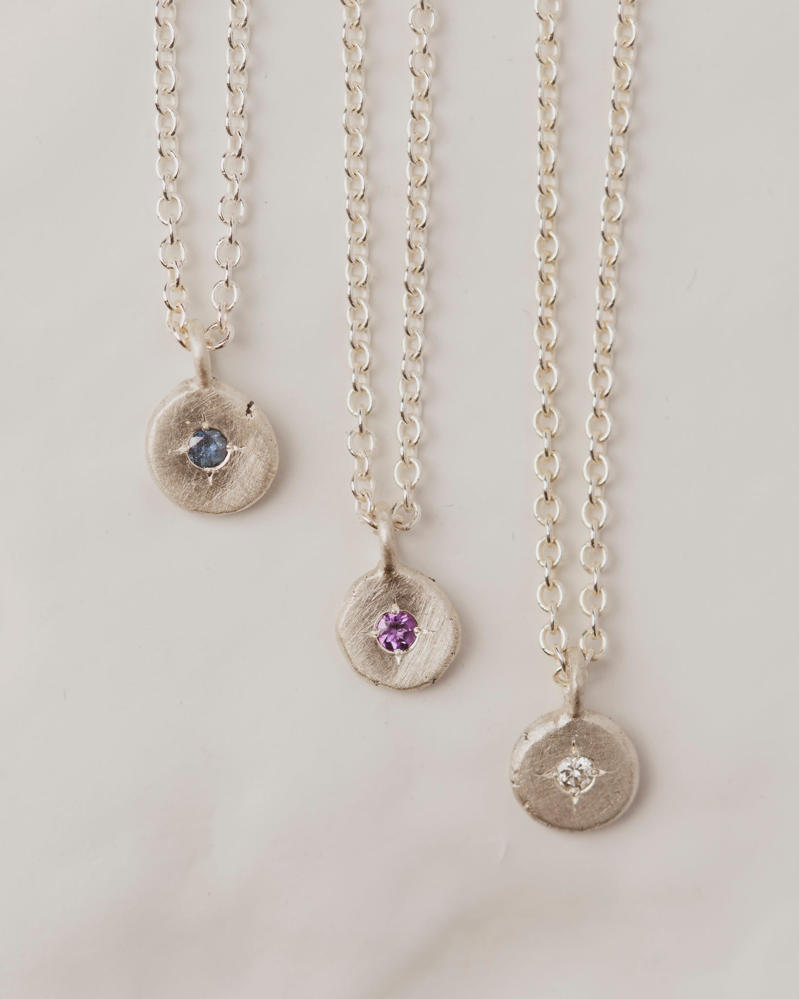 These sterling silver pebble gemstone necklaces have a 2mm diamond, sapphire, or amethyst in the center.