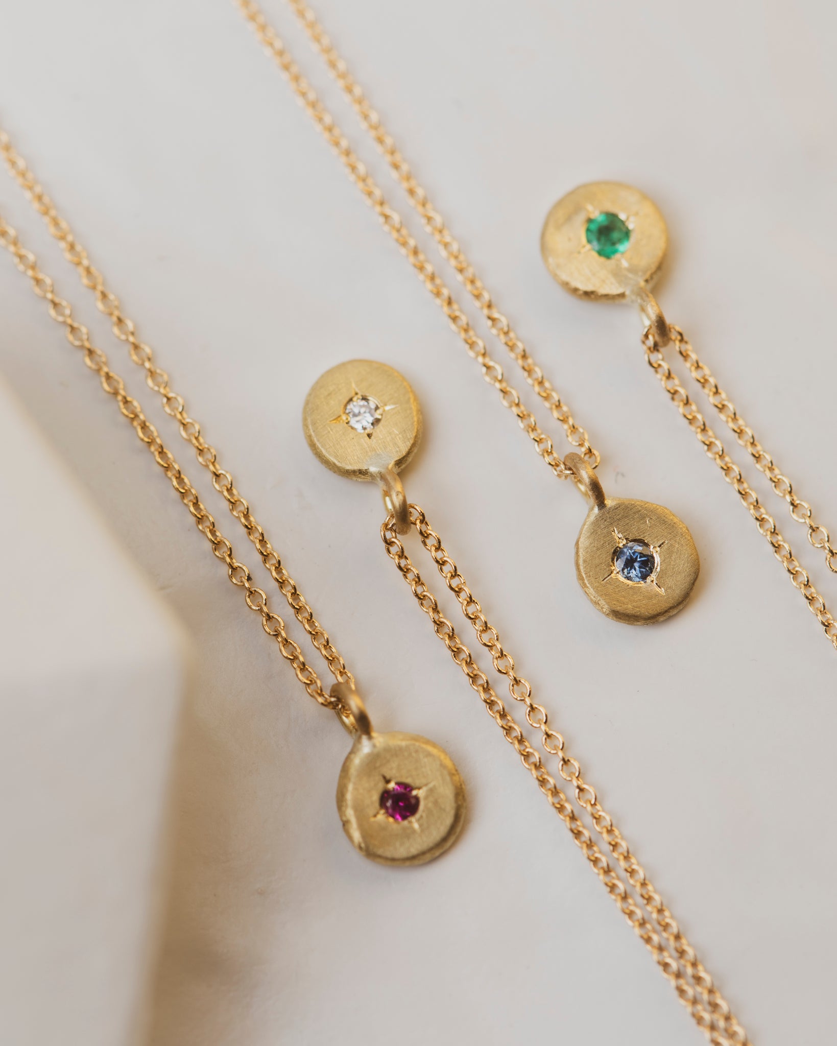 18K yellow gold pebble gemstone necklaces with a diamond, sapphire, emerald or ruby in the center. 5mm round with 2mm gemstone