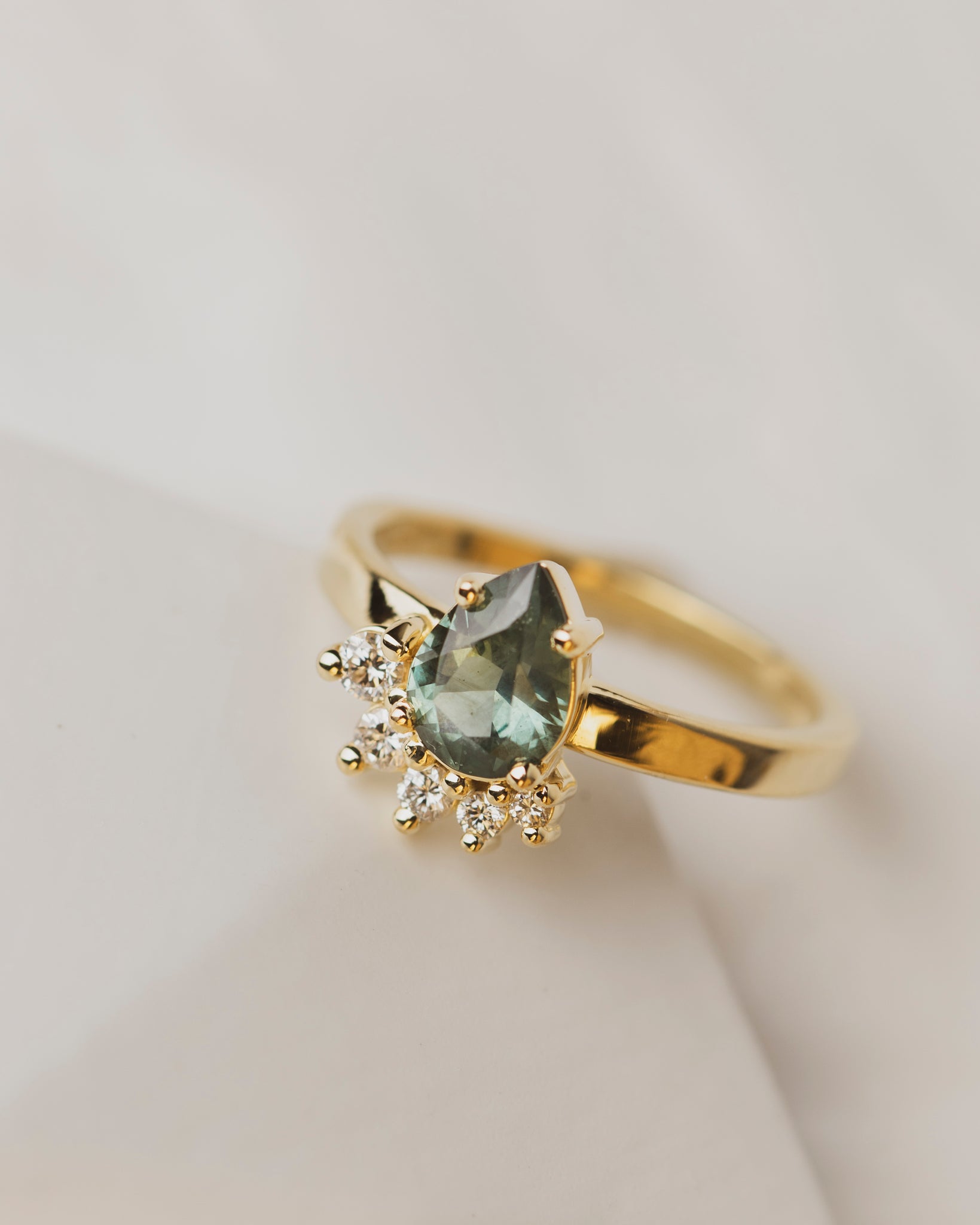 Our signature Pear Wave style engagement ring boasts a 1.2 carat green sapphire from Australia with a wave of five white diamonds set in 18K yellow gold