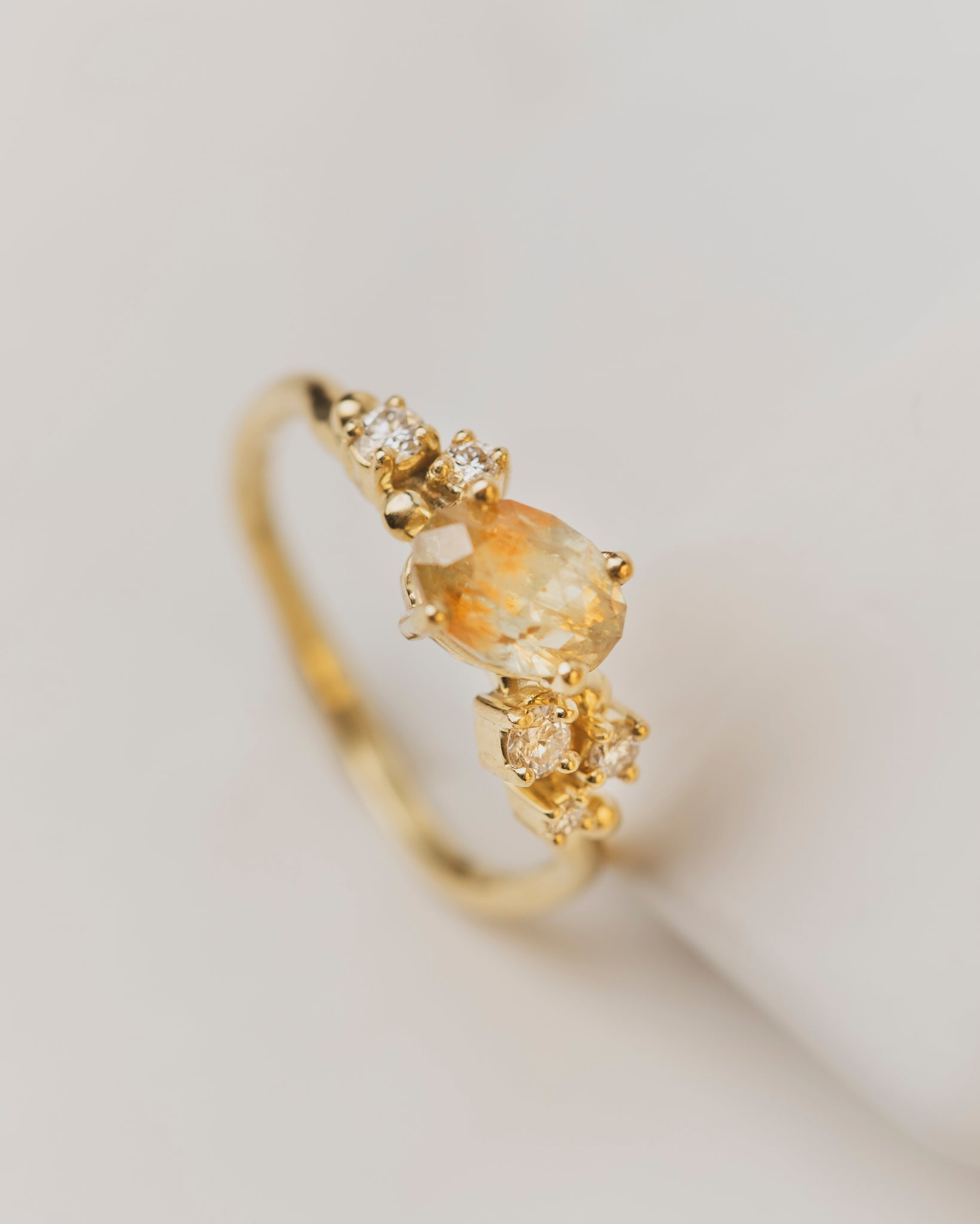 This 1.52 carat yellow and orange hued sapphire is nestled in a cluster of five white diamonds set in 18K yellow gold